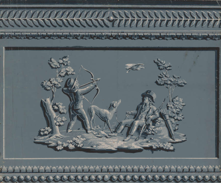 Gray rectangular panel with an elaborate decorative border and raised hunting scene of two figures, one standing holding an arrow aimed at a bird in flight and the other sitting.