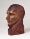 Three quarter front view of a vibrant, carved wood sculpture depicting a serene face wearing a draped cloth around its head. It is smooth, besides a vertical crack alongside its nose.