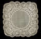 Square of fabric with rounded edges and a lacy border. The surface features intricate embroidery depicting intertwined curving lattices around delicate flowers surrounding a circle of plain fabric.