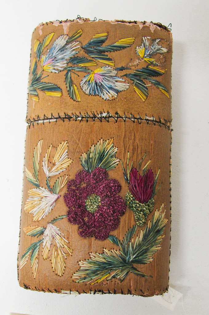 Tan rectangular case. The cap of the case has green, yellow, and blue floral embroidery while the case’s body features pink, yellow, and green floral embroidery.