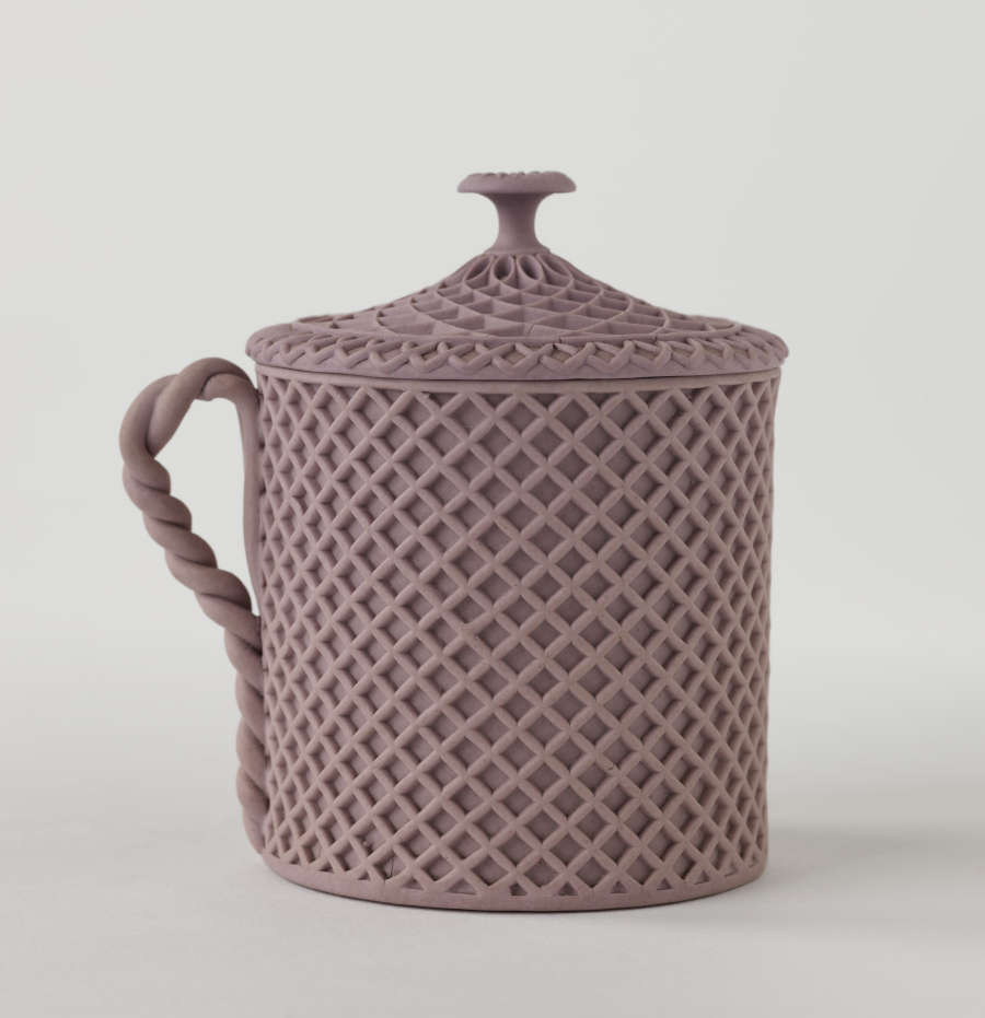 A purple covered cup with raised woven texture. The handle is sculptural and swirled.