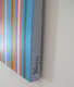 Angled view of a striped painting featuring narrow vertical bands in bright blue, black, red, white, and yellow. The canvas edge is painted grey and signed “Riley ‘81.” 