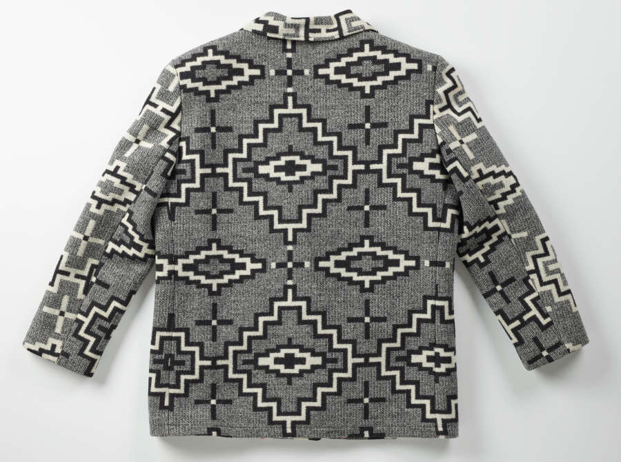 Back of a gray tweed blazer with black and white geometric designs. The geometric patterns oscillate between white diamond-shaped motifs surrounded by black-bordered white zig-zag designs, and black crosses.