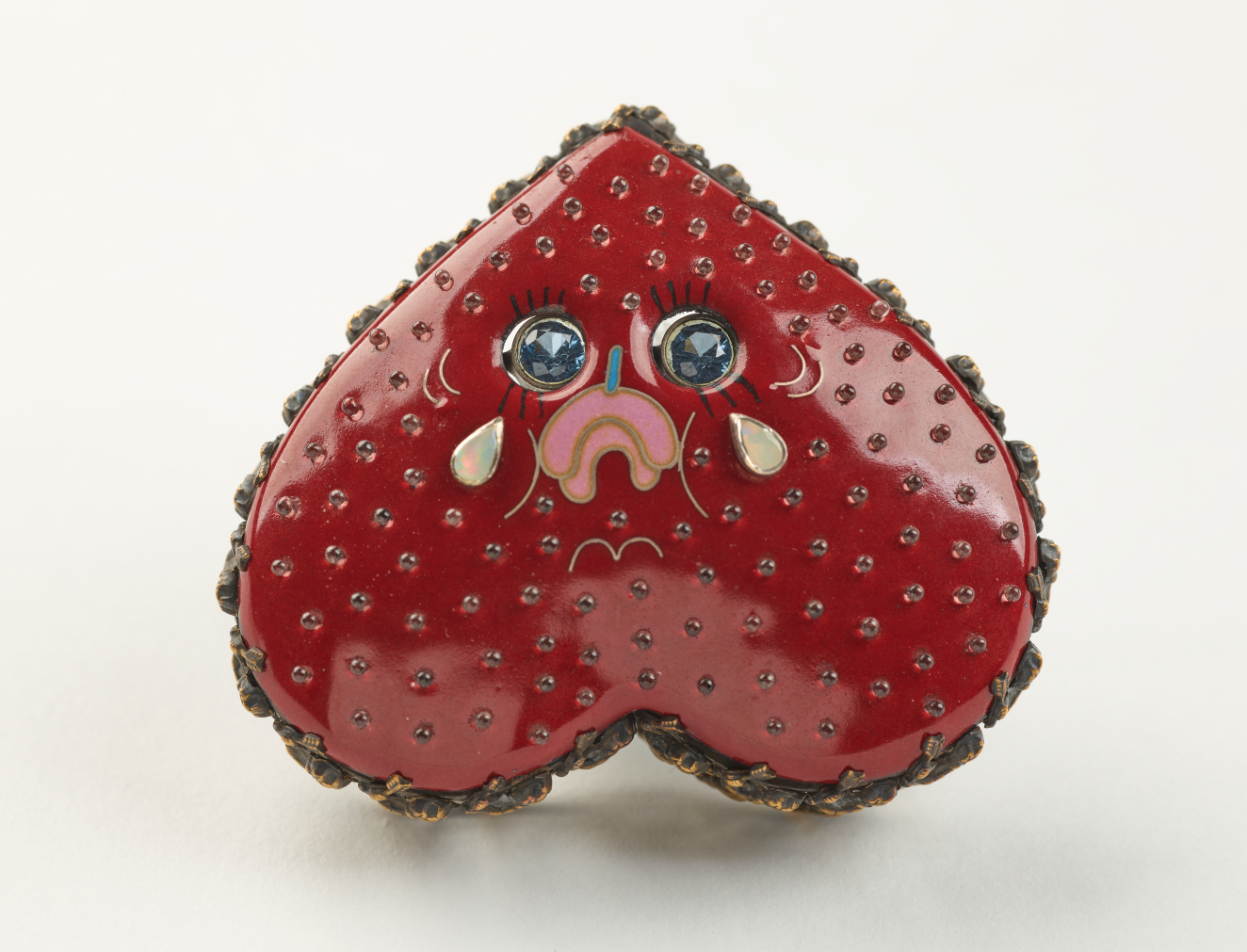 Brooch shaped like an upside-down heart with a cutesy sad frowny face tearing up. The glossy red surface speckled with small metallic dots.