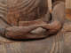 The hands of a wooden Buddha statue resting in its lap, with its fingers forming a circle with the weathered wood showing deep cracks and rough textures.