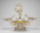 Elaborate silver double-oval-tray centerpiece with central fountain-like stem topper of winged-figurine holding up a suspended gold garland, surrounded by cherubs, framed by swirling arms extending to two shallow dishes.