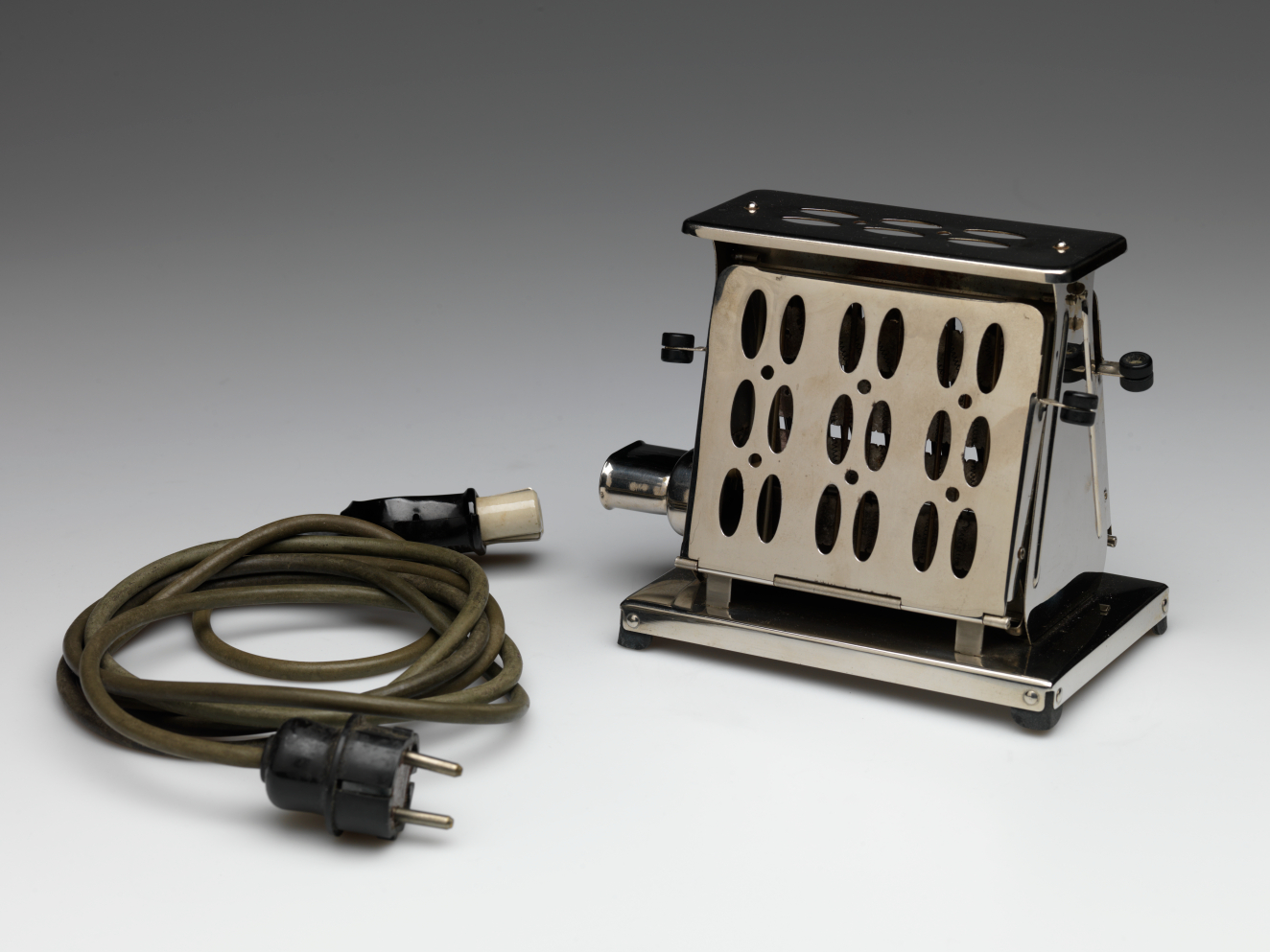 A metal toaster with perforated sides and black accents, displayed with a detachable two-prong green electrical cord.