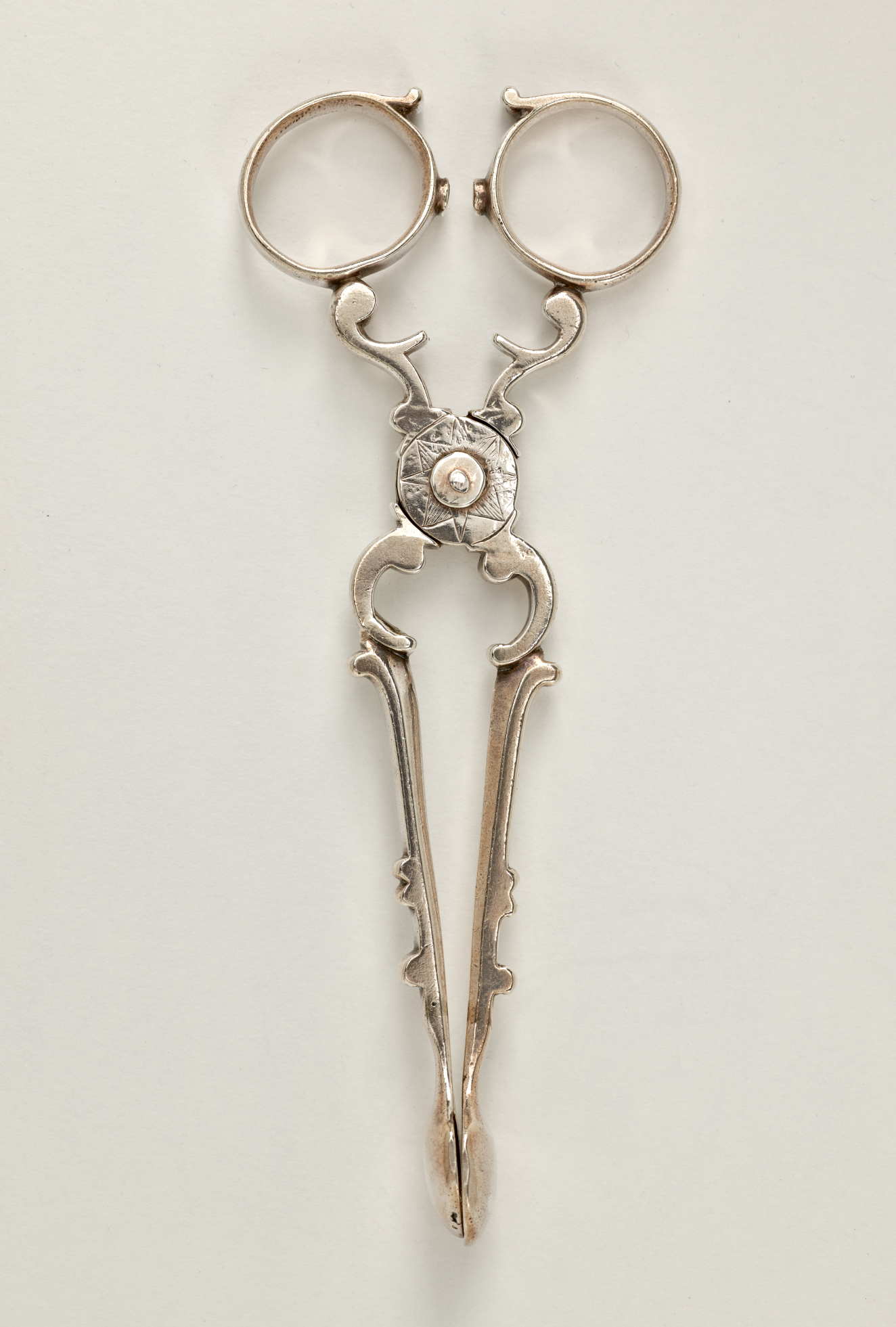 Silver sugar tongs that are delicate and swirled.