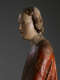 A profile view of a weathered wooden statue of a figure with a solemn expression, with red and green drapery.