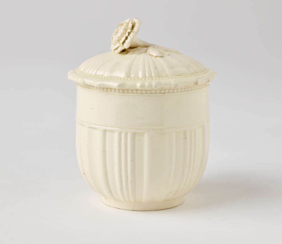  A cream-colored cup with a sculptural swirled handle, and lid with sculpted finial.