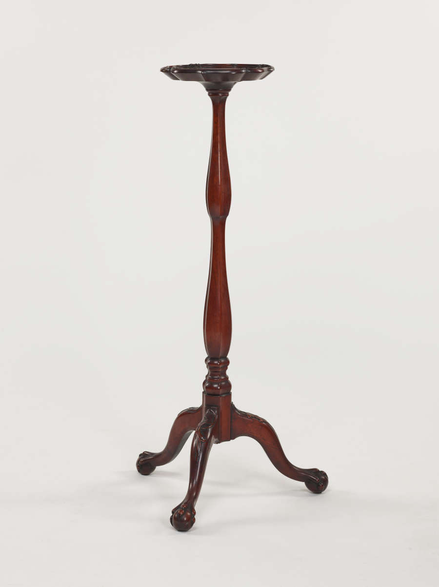 A tall, wooden candle stand with turned legs and ornate, tripod feet.