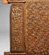A close up of a carved wooden panel, with intricate calligraphic inscriptions bordered by interlocked geometric floral designs.