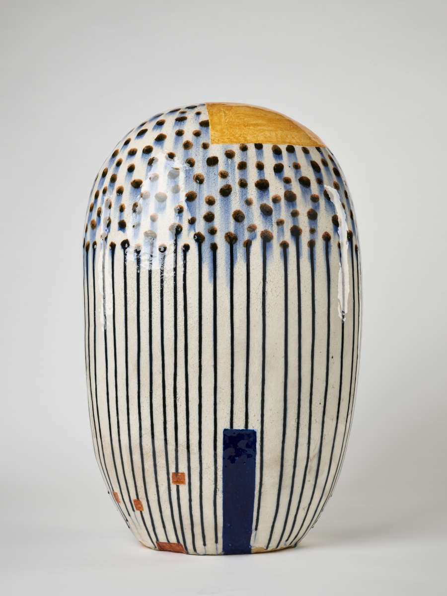 Organic cylinder form glazed in white with black dots on the top that smudge and bleed, forming vertical black stripes. A yellow ochre patch partially covers the top.