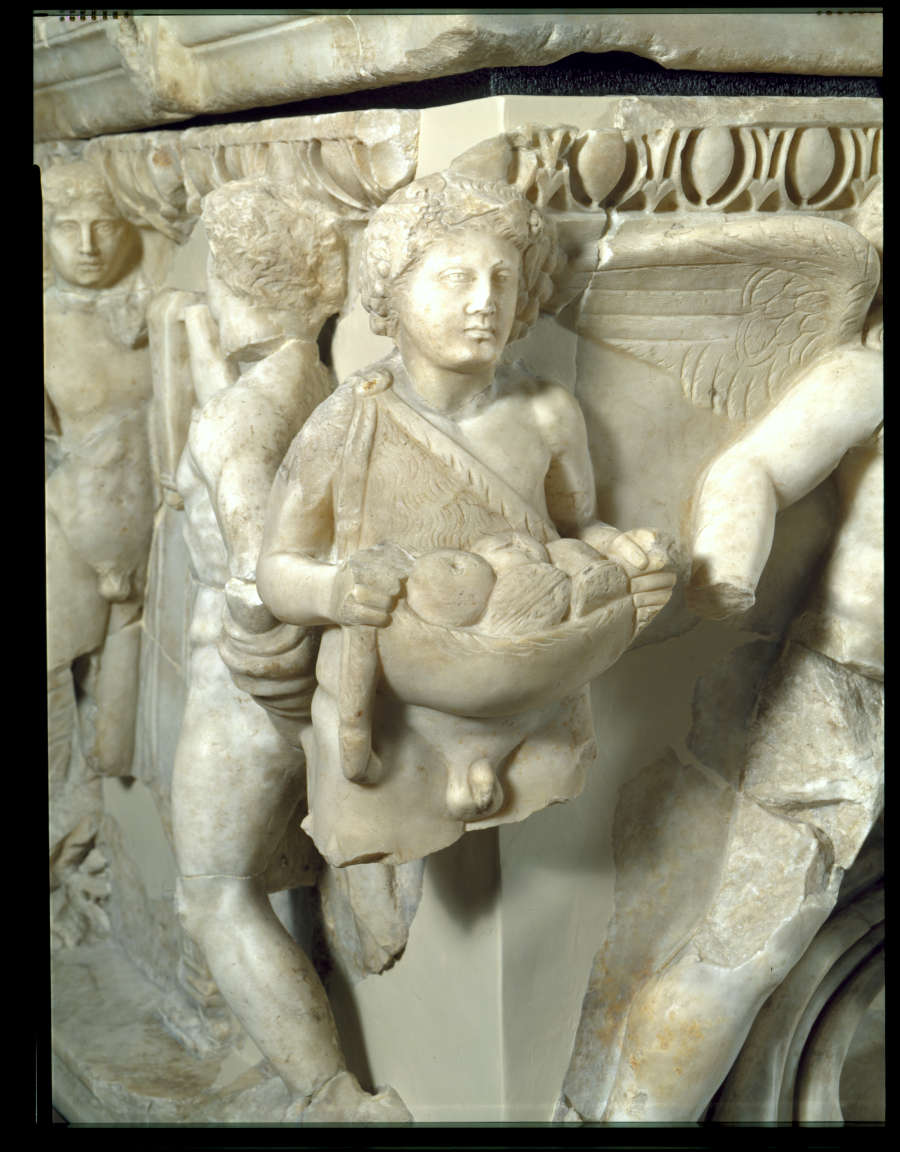 A detailed carving on a marble corner of a young figure carrying a bowl of fruit, draped in a sash, with a winged figure in the back.