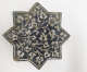 A gray-blue eight-pointed star tile with a white border detail and symmetrically-arranged white floral patterning emerging from one point.