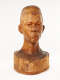 Slightly angled view of a glossy wooden bust depicting the head of a male figure with afrocentric facial features. He has a stern expression and an intense gaze.
