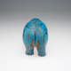 Rear view of bright blue ceramic hippopotamus. A delicate black-painted flower curves symmetrically up its back, with areas of worn-down glaze exposing brownish ceramic beneath.