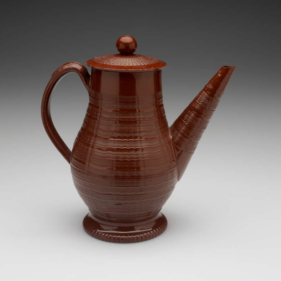 A brown coffee pot with a long straight spout, handle, foot, and lid with decorative horizontal grooves and projecting grooves. The final which is spherical in shape.