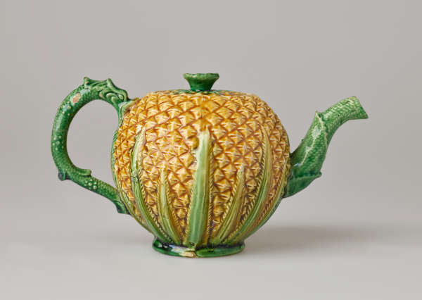 A teapot in the shape of a pineapple. Handle, foot, lid, and spout are green.