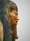 Side view of a coffin with a gilded face, beard, blue outlined eyes and a blue-black headdress with gold detailing. 