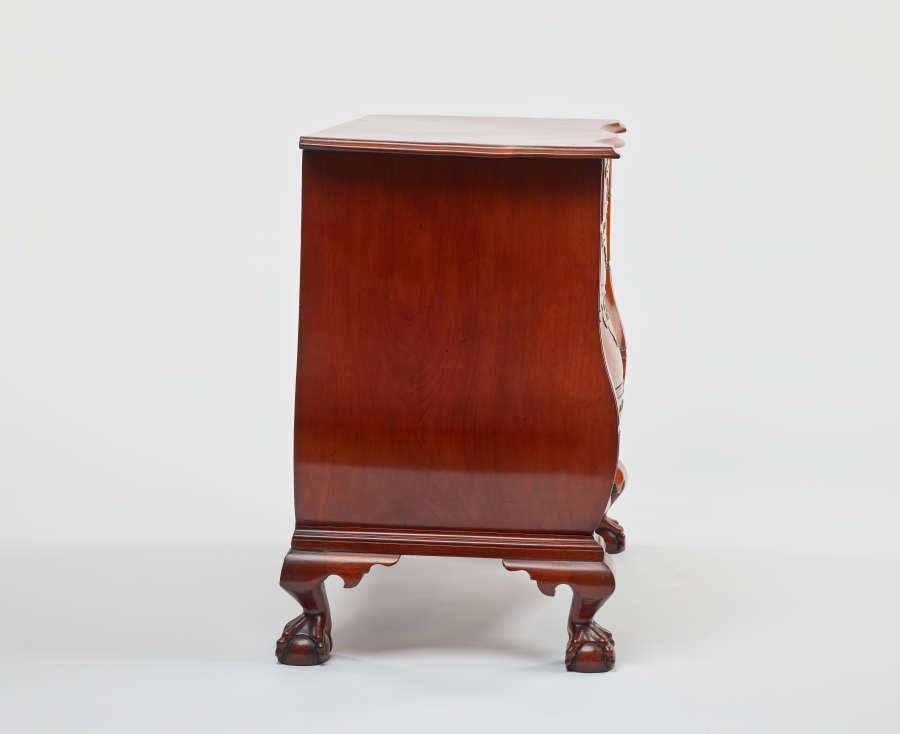 Side view of a polished wooden dresser with curved edges, resting on ornamental, carved claw feet.