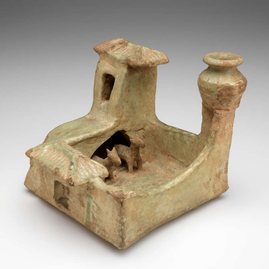 A worn pale-green ceramic sculpture of a farmyard with a courtyard with two animals and two towers, one with a room, and another with a pot upon it.