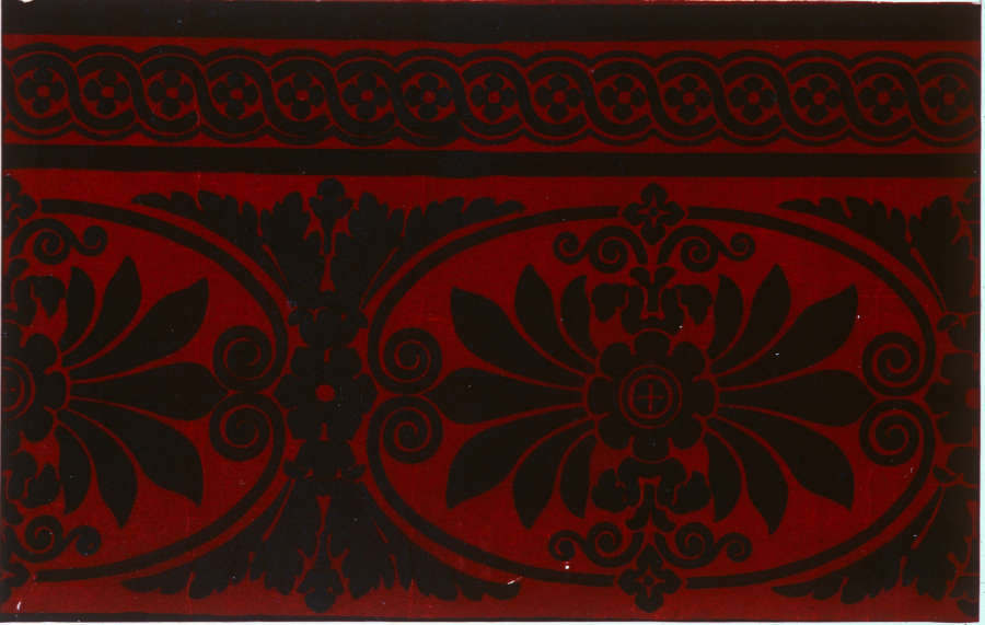 Black floral ornamentation in oval shapes with intricate scrolls on a deep red background. A thinner section of interwoven circles sits at the top.
