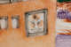 A close up of a painted ceramic depicting an orange wall with a window with an illustrated face, surrounded by smaller plain rectangular windows.