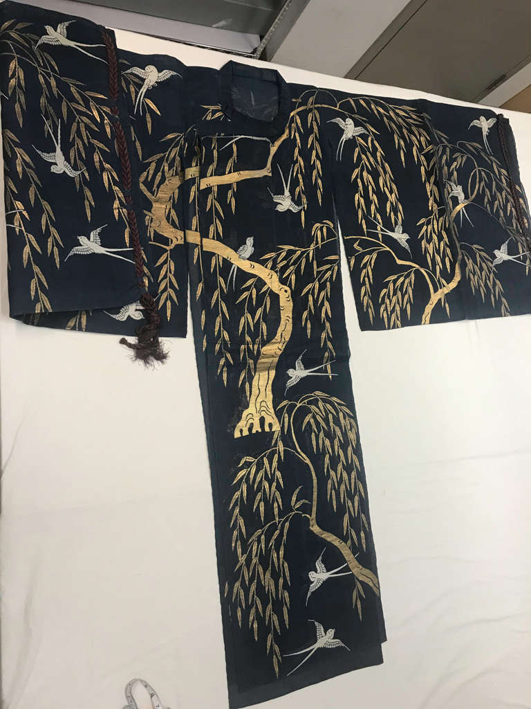 A dark blue kimono adorned with gold willow trees and white birds, displayed flat on a white surface.