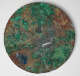 Front of an ornate circular mirror, with a surface corroded into moss-like blues, greens, and browns. A small white rectangular label reading “2007 90-10” is placed near the center.