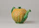 A teapot in the shape of a pineapple. Handle, foot, lid, and spout are green.