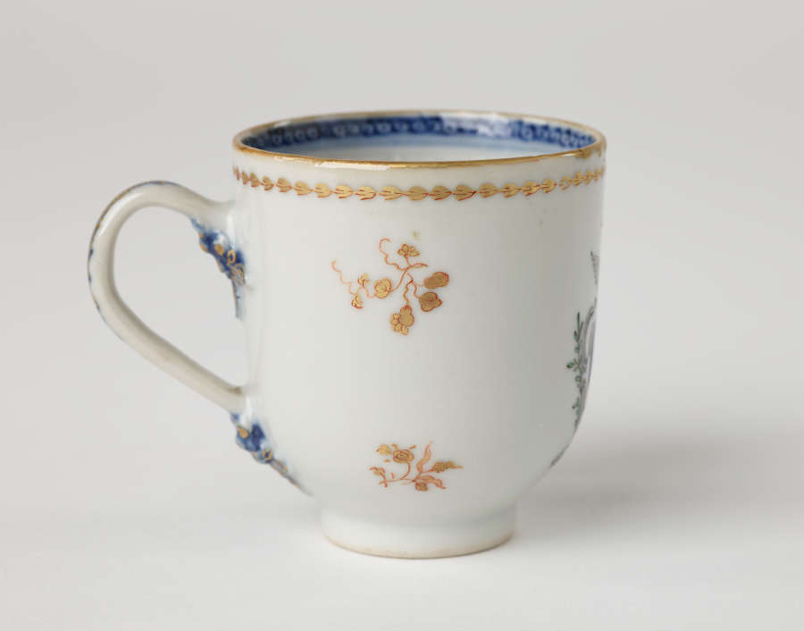 A cup with blue and gilded decorations along the outside and inside of the rim, body, and handle.