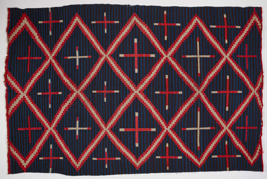 Striped navy blue blanket with three, different sized, alternating cross patterns: red crosses, red with white tips, and white with red tips, within a red and cream three-striped diamond pattern.