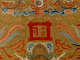 A bold red Chinese character enclosed in a square frame, surrounded by golden medallions, stylized clouds and red flames.