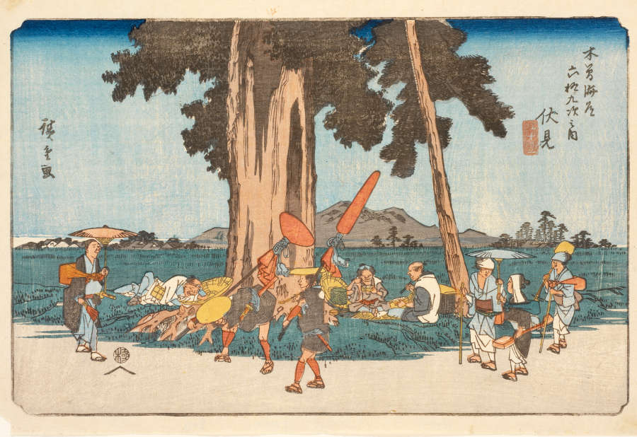 A polychrome woodblock print of travelers gathering under the shade of a large cedar in a green field. People pass in front of the tree with umbrellas and assorted baggage.