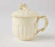  A cream-colored cup with a sculptural swirled handle, and lid with sculpted finial.