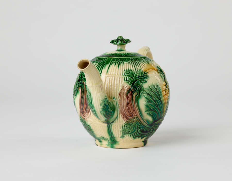 A bulbous teapot with white, green, and yellow floral decorations in the form of a leafy pineapple.