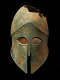 Bronze helmet with a narrow nose guard and sharp eye holes. The corroded surface is brown with significant green discoloration. The top has jagged sections missing along the crown.