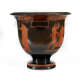 Stout black bowl with a wide striped foot and flared patterned mouth. Visible is one sloping handle, and orange illustrations of figures emerging from  negative space below the handle.