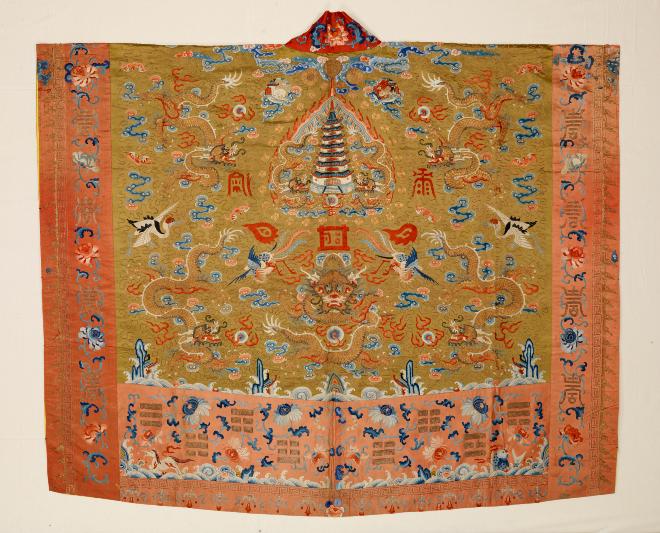 An ornate, orange robe with a rectangular panel in golden yellow depicting a central pagoda, dragons and birds in gold, blue, and red, with a lower section of embroidered calligraphy.