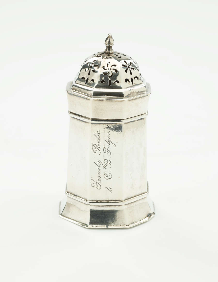  A silver vessel that has an octagonal body, handle, and lid that has floral perforations.
