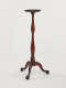 A tall, wooden candle stand with turned legs and ornate, tripod feet.