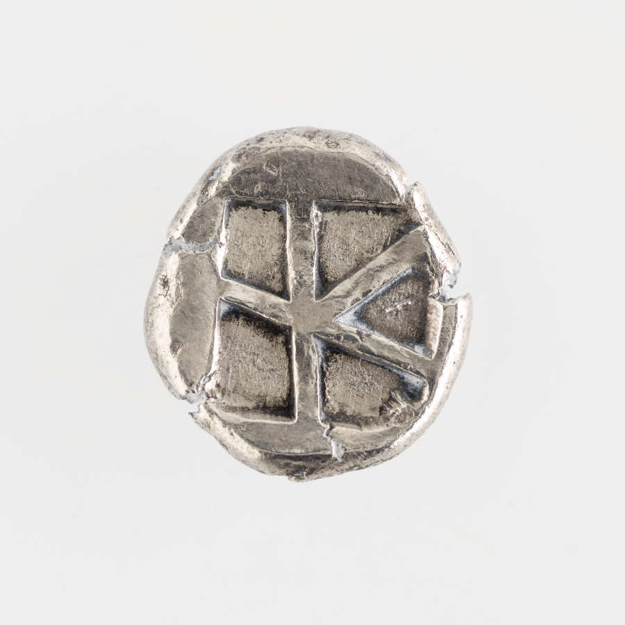 Silver coin with irregular edges. Embossed on its surface is a star-like shape dividing a square into five regions.