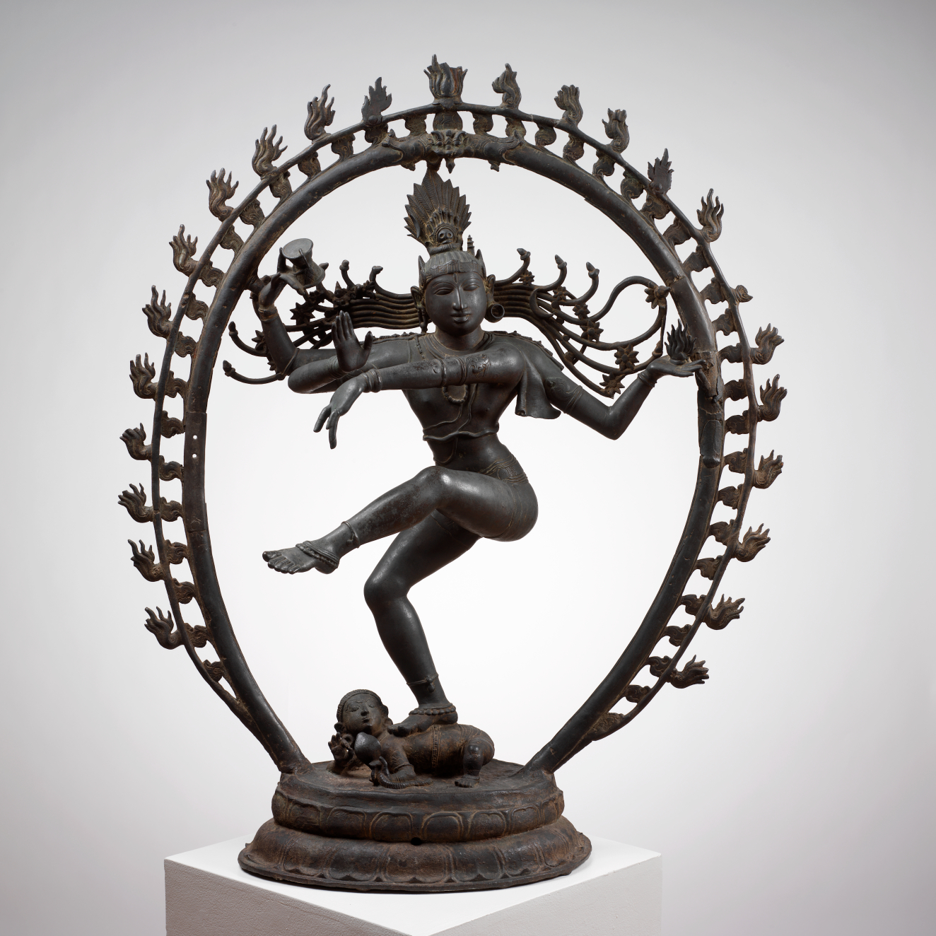 The Hindu god Shiva dancing within a flaming circle. His raised foot and flowing hair suggest movement, while multiple hands gesture and hold objects. He stands on a small figure.