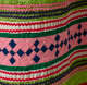 Detail of the pattern. A thick strip of pink with blue squares woven through it is surrounded by wavy horizontal green,white, and red stripes. 