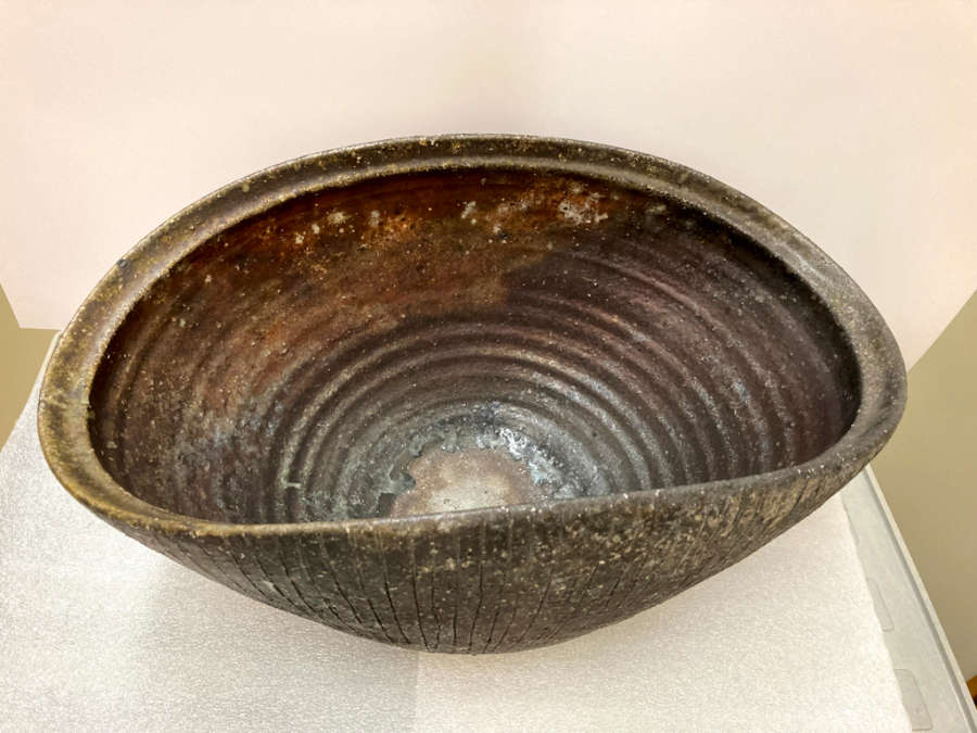 Partial top-view of an oblong bowl with circular ridges on the inside. The outside of the bowl has shell-like etchings and sides that dip to form a wave-like shape. 