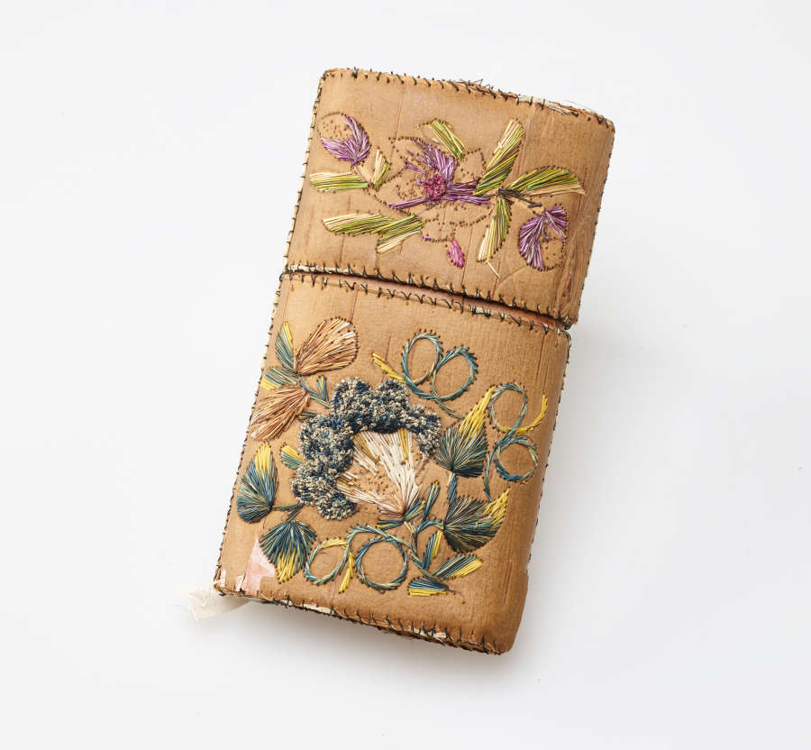 Tan rectangular case. The cap of the case has green, yellow, and blue floral embroidery while the case’s body features pink, yellow, and green floral embroidery.