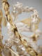 A silver figure with golden wings holds her wavy, tangled hair with one hand and a long gold garland aloft in the other hand with trumpet-blowing cherubs around her. 