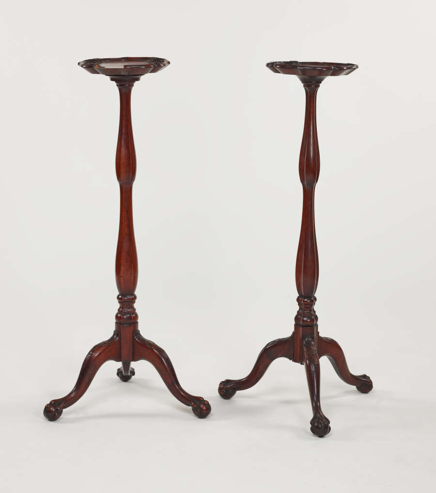 A pair of tall, wooden candle stands with turned legs and ornate, tripod feet.