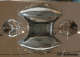 Bottom view of sculptural silver form with mirror-like curved reflective surfaces, rounded ends, ornate swirls, and a recessed rectangular base. 